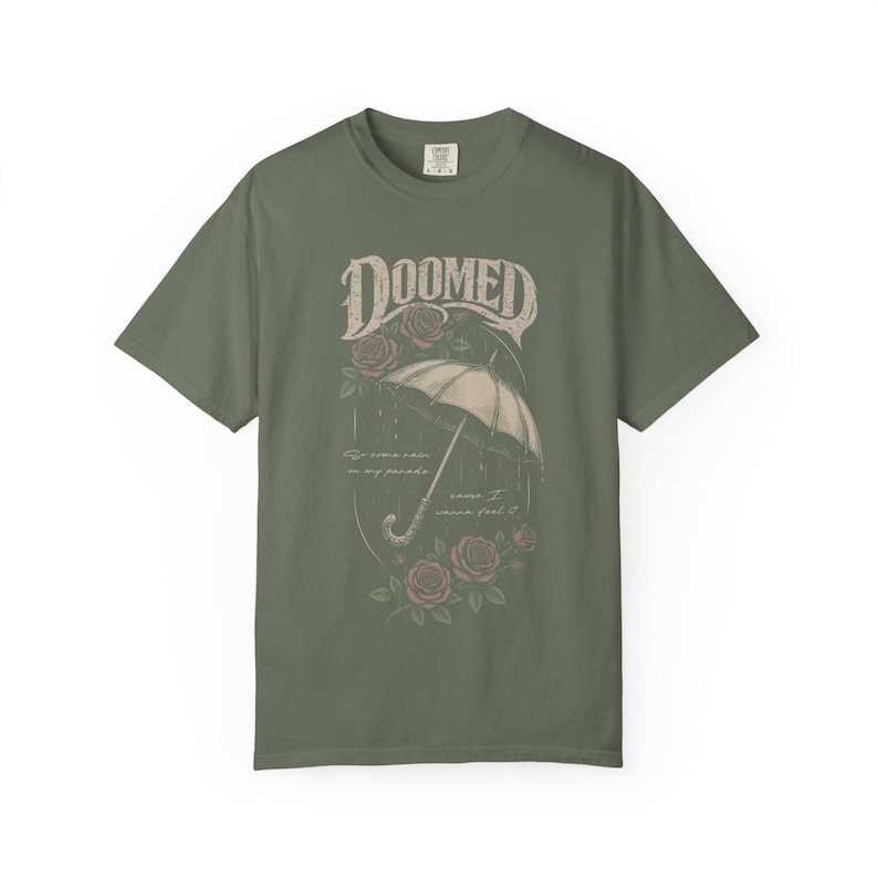 moss color Comfort Colors T-shirt featuring a vintage gothic umbrella illustration with roses and rain details and the word “Doomed” in distressed lettering.