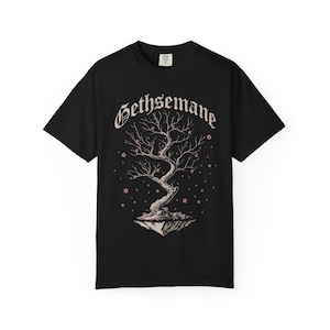 May include: A black short-sleeve t-shirt featuring a graphic print of a gnarled tree on a floating island. The word Gethsemane is printed in a gothic font above the tree, which is surrounded by small pink cherry blossoms and falling petals.