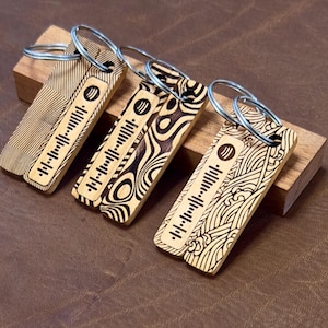 Puede incluir: Cuatro llaveros de madera con diferentes patrones y un diseño de código de barras en blanco y negro. Los llaveros están sobre una superficie de madera.