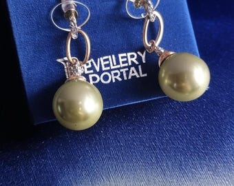 May include: A pair of gold-toned earrings with olive-green pearl-shaped drops. The earrings have a post-and-loop design with a small, clear stone accent. The text "JEWELLERY PORTAL" is visible on the blue box.