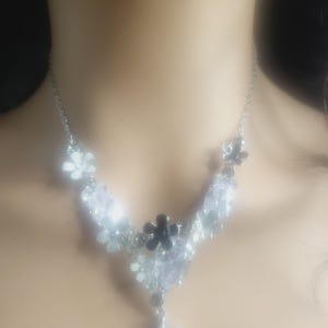 May include: A silver necklace with a teardrop pendant and a cluster of silver and black flower-shaped charms.