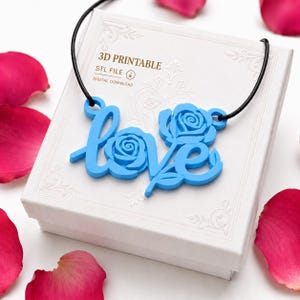 May include: A bright blue pendant featuring the word love with rose motifs integrated into the letters, suspended on a black cord. The pendant rests on a white box labeled 3D PRINTABLE STL FILE DIGITAL DOWNLOAD, surrounded by scattered pink rose petals.