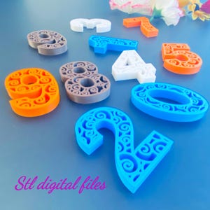 Könnte beinhalten: Eine Sammlung dreidimensionaler Zahlen mit komplizierten, wirbelnden Filigranmustern. Das Set enthält verschiedene Ziffern in den Farben Orange, Blau, Weiß und Grau. Der Text "Stl digital files" ist unten links in Pink aufgedruckt.