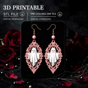 Può includere: Un paio di orecchini pendenti con una figura di fantasma bianco centrata all'interno di una cornice in filigrana rosa polvere. Ogni orecchino include una piccola perla rosa e un gancio dorato. Il testo 3D PRINTABLE, STL FILE e 3MF FILE è visibile.