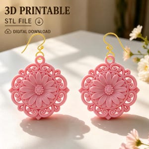 May include: A pair of pink circular earrings featuring a central daisy motif surrounded by intricate scrollwork patterns. The earrings are suspended from gold-toned metal hooks. The text 3D PRINTABLE STL FILE and DIGITAL DOWNLOAD is visible.