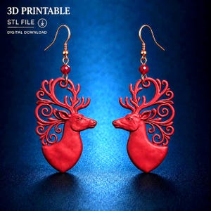 Può includere: Un paio di orecchini rossi con la sagoma di una testa di cervo e disegni di corna con volute ornamentali. Ogni orecchino pende da un gancio dorato con una piccola perla rossa. Il testo 3D PRINTABLE STL FILE DIGITAL DOWNLOAD è visibile.