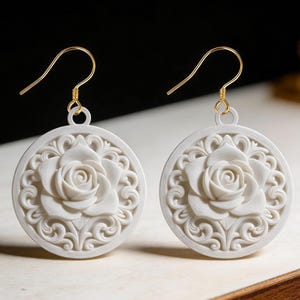 May include: A pair of white, circular earrings with a detailed rose design. The earrings have gold-colored hooks and intricate, swirling patterns around the rose. The earrings are a delicate, floral accessory.