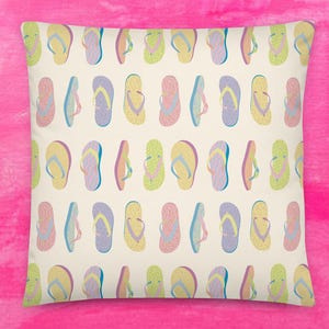 May include: Square throw pillow with a repeating pattern of colorful flip-flops in shades of yellow, pink, blue, and green on a cream background. The pillow is set against a bright pink backdrop.