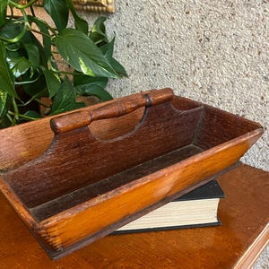 May include: A rectangular wooden caddy with a central handle and a dark brown finish. The tray features a deep, open compartment design with visible wood grain and a smooth, polished surface, constructed with sturdy sides and a base.