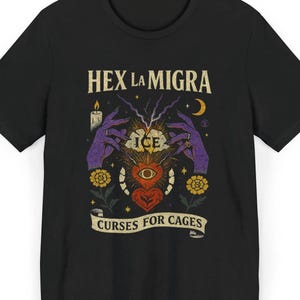 May include: Black t-shirt with a graphic design featuring the text "HEX LA MIGRA" above an illustration of hands, a heart, and the text "CURSES FOR CAGES". The design includes a candle, lightning bolts, and a crescent moon.
