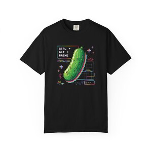 Op de afbeelding: Zwart T-shirt met een gepixeld groene augurk ontwerp. Het ontwerp bevat de tekst "CTRL + ALT + BRINE" in een retro, digitale stijl. De augurk staat centraal, met een levendige, kleurrijke omtrek.