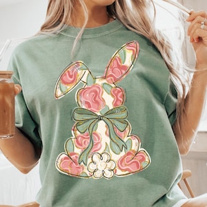 May include: A green t-shirt with a floral bunny graphic. The bunny is pink, green, and yellow with a green bow.