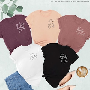 May include: A collection of t-shirts in various colors, including maroon, peach, white, and black. Each shirt features elegant script text, with phrases like "Mother of the Bride," "Aunt of the Bride," "Bridesmaid," "Bride," and "Bridesman."