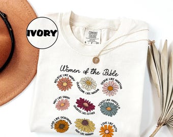 May include: Ivory-colored t-shirt with the text "Women of the Bible" and floral illustrations. Each flower represents a biblical woman, such as Mary, Sarah, and Ruth. The shirt has a crew neck and short sleeves.