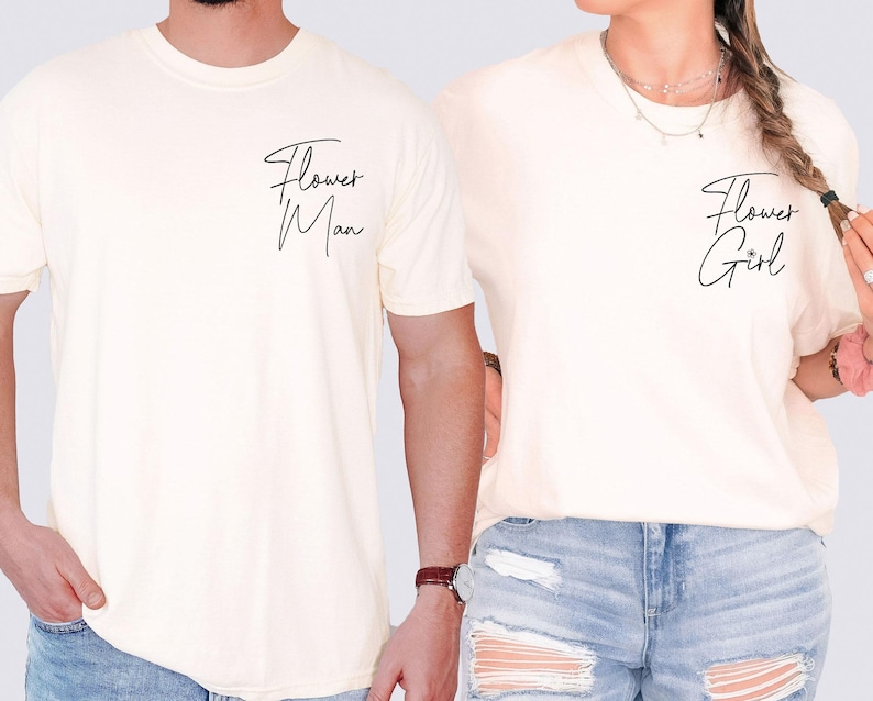 May include: Cream-colored t-shirts with the phrases "Flower Man" and "Flower Girl" in black script. The shirts are short-sleeved and appear to be made of a soft material. The shirts are worn by two people.