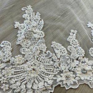 Op de afbeelding: Witte bruids sluier met een parelversierde kant rand. De kant heeft een bloemmotief met parel-achtige versieringen.