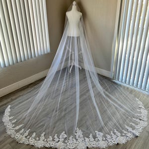 Op de afbeelding: Een witte bruids sluier met een delicate kantversiering. De sluier is lang en vloeiend, met een zachte tule stof.