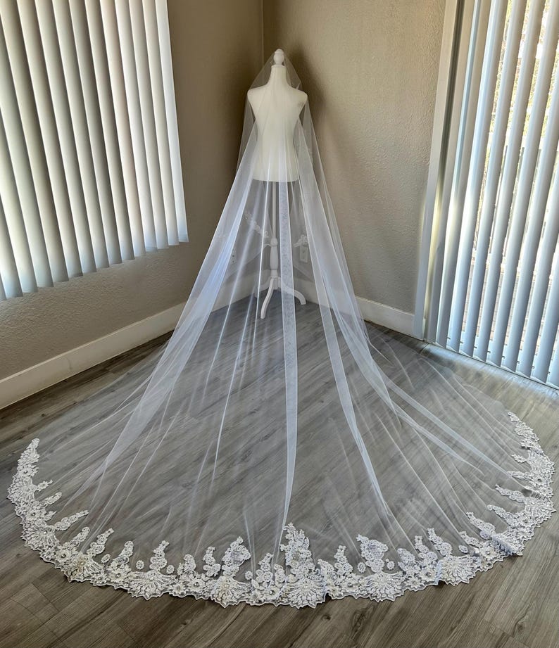 Op de afbeelding: Een witte bruids sluier met een delicate kantversiering. De sluier is lang en vloeiend, met een zachte tule stof.