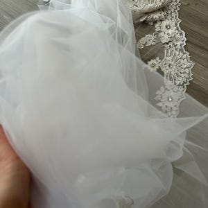 Op de afbeelding: Witte tule bruids sluier met delicate kant versiering en parel versiering.