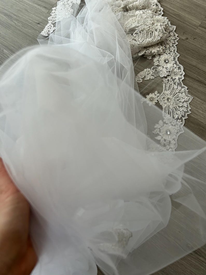 Op de afbeelding: Witte tule bruids sluier met delicate kant versiering en parel versiering.