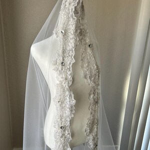 Op de afbeelding: Een witte bruids sluier met een parelversierde kantbies. De bies heeft een bloemmotief met strass.