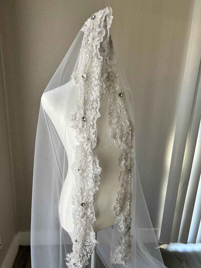 Op de afbeelding: Een witte bruids sluier met een parelversierde kantbies. De bies heeft een bloemmotief met strass.