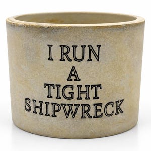 May include: A cylindrical beige ceramic planter with a weathered, stone-like texture. The front surface features the black, capitalised text "I RUN A TIGHT SHIPWRECK" printed in a bold, serif font. The vessel has a wide, open top and a flat base.