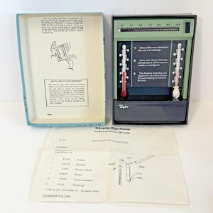 May include: A vintage Taylor Eduquip-Macalaster psychrometer kit. The kit includes a green and black instrument with two thermometers, a roll chart, and instructions. The box is light blue. The thermometers show red liquid.