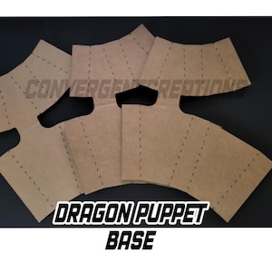 以下が含まれることがあります： 黒い背景に配置された、点線のある茶色の段ボールの切り抜き。テキスト「DRAGON PUPPET BASE」は白で表示されています。切り抜きはドラゴンパペット用です。