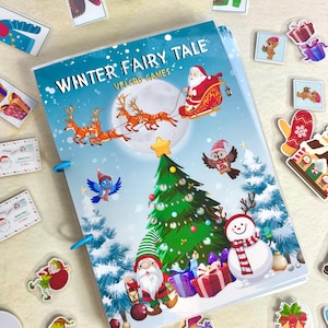 Op de afbeelding: Een "Winter Fairy Tale" Velcro Games boek met een blauwe kaft met de kerstman in een slee getrokken door rendieren, een kerstboom en een sneeuwman. Diverse kerststickers liggen verspreid.