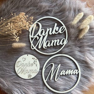 Könnte beinhalten: Drei Holz Kreise mit den Worten "Danke Mama" und "Mama" in Kursivschrift. Die Kreise liegen auf einer grauen, flauschigen Oberfläche.