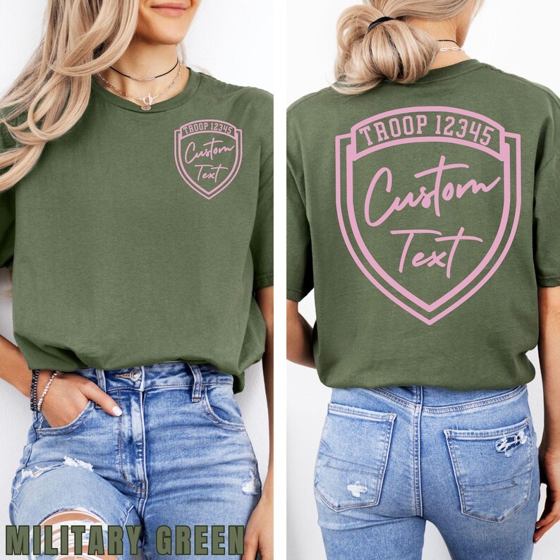 A woman wearing a green t-shirt with a shield-shaped logo and text on the back, paired with distressed jeans.