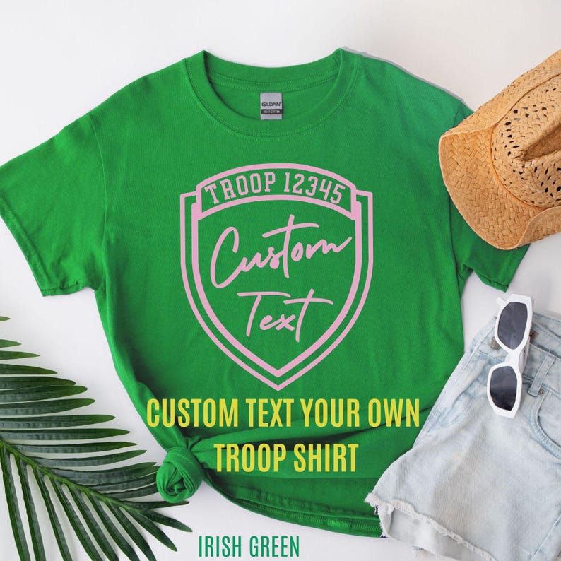a green T-shirt with a custom text design, a straw hat, sunglasses, and some denim shorts, all arranged on a white background.