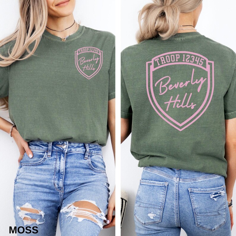 A woman wearing a green t-shirt with a shield-shaped logo on the back, and distressed jeans.