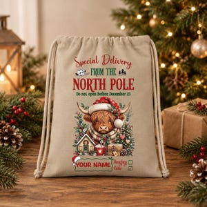 Può includere: Una borsa in tela beige con coulisse e il testo Special Delivery FROM THE NORTH POLE Do not open before December 25. La grafica mostra una mucca Highland con un cappello da Babbo Natale, una casetta, una tazza e un regalo. YOUR NAME è stampato sotto.