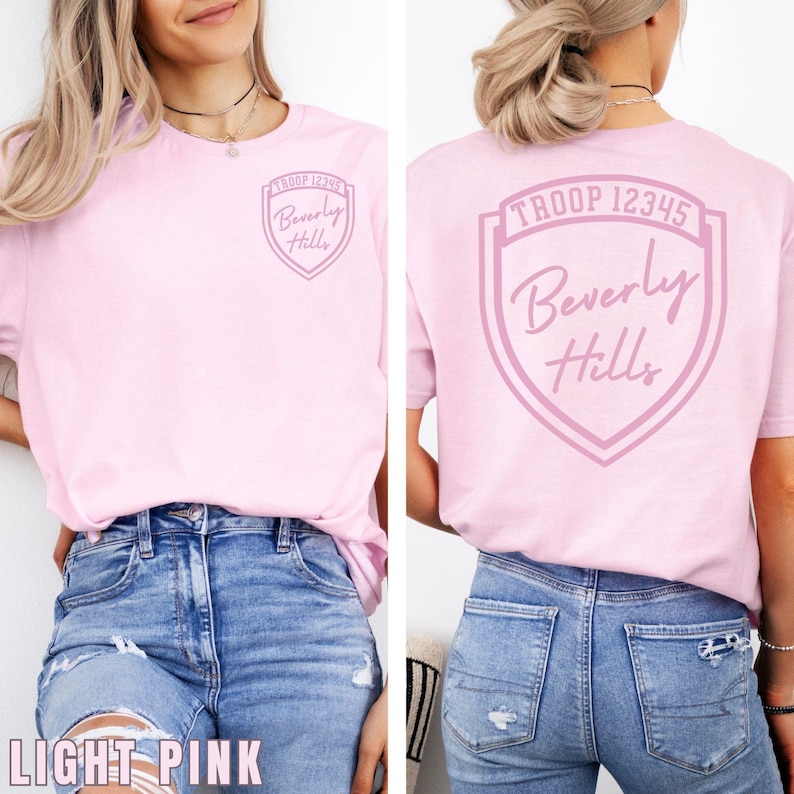 A woman wearing a pink t-shirt with a shield design and text on the back.