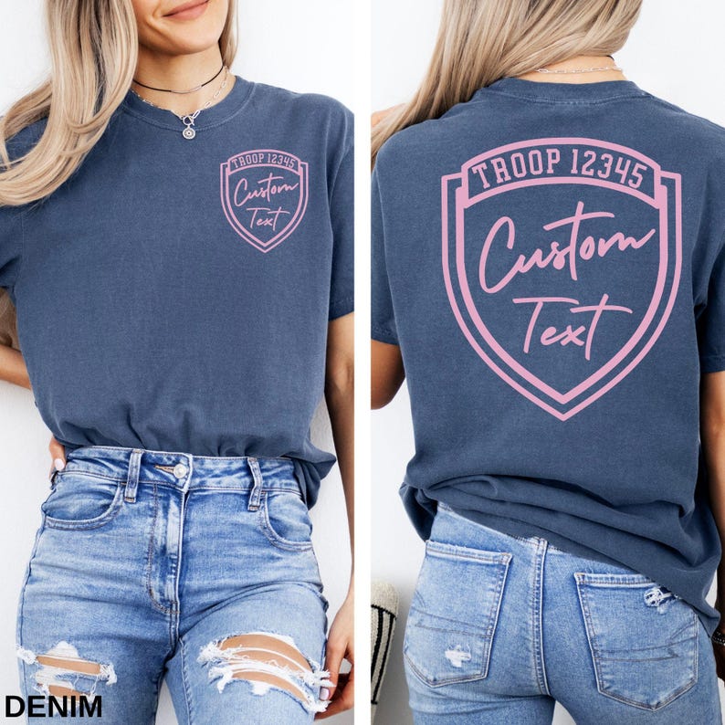 A woman wearing a blue t-shirt with a pink shield design and text on the back, paired with distressed jeans.