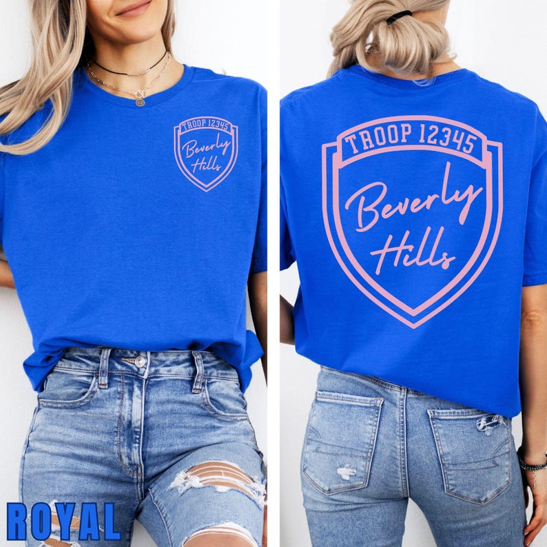 A woman wearing a blue t-shirt with a shield design and text on the back, paired with distressed jeans.