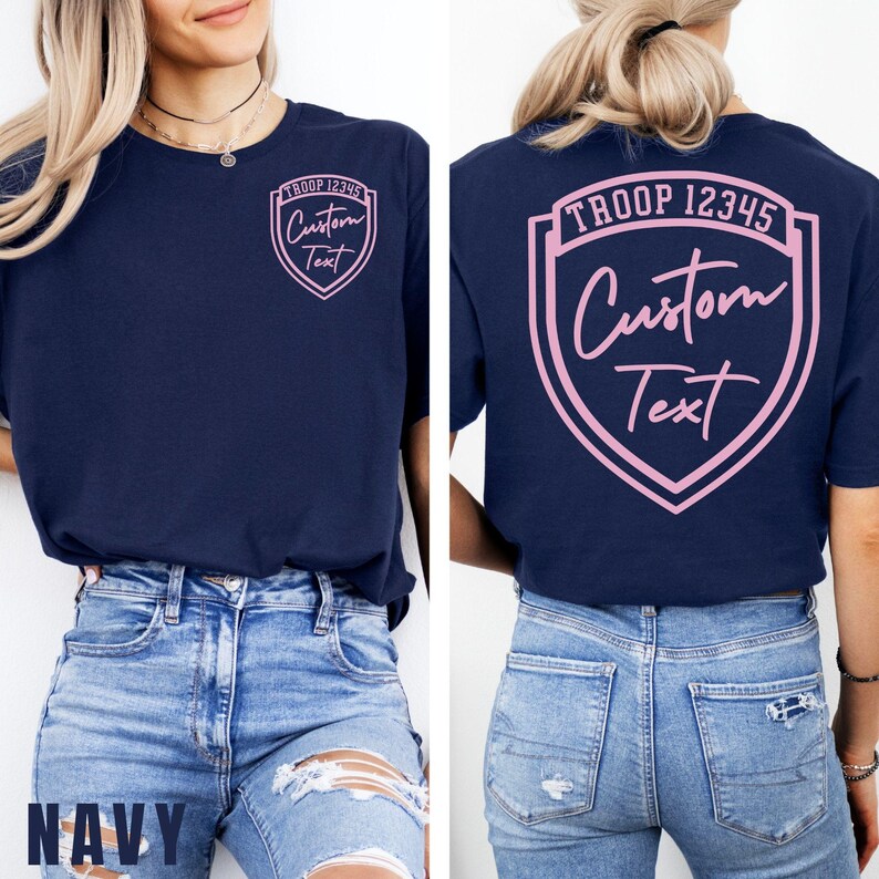 A woman wearing a navy blue t-shirt with a pink shield design and text on the back, paired with distressed blue jeans.
