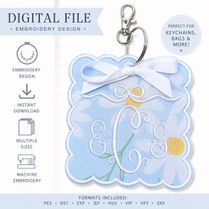 May include: A light blue, scalloped-edge keychain with a daisy pattern and the embroidered letters "E" and "C". It has a white ribbon and a silver-colored clasp. The text "DIGITAL FILE - EMBROIDERY DESIGN" is at the top.