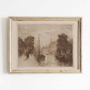 May include: A sepia-toned framed print depicting a waterside scene with boats, trees, and buildings. The artwork has a vintage aesthetic, with soft details and a muted color palette. The frame is a light, neutral color, complementing the artwork's tones.