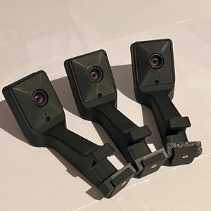 May include: Three black, rectangular devices with a lens and a long handle. Each device has a small, circular lens. The handles have a rectangular base. The devices are arranged in a row.