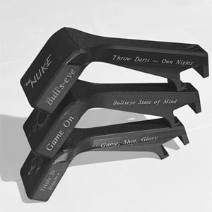 May include: Black dart accessories with engraved text. The top piece reads "THE NUKE" and "Bull's-eye". The middle piece says "Bullseye State of Mind". The bottom piece says "Game, Shot, Glory". The accessories are stacked on top of each other.