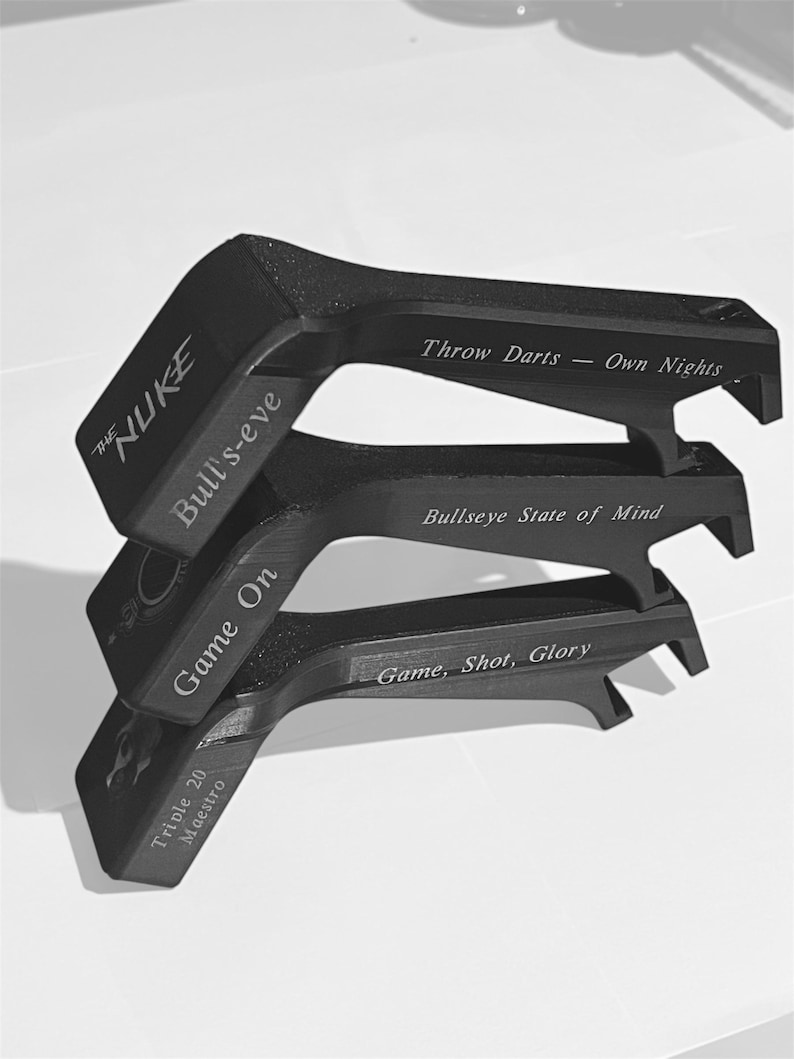 May include: Black dart accessories with engraved text. The top piece reads "THE NUKE" and "Bull's-eye". The middle piece says "Bullseye State of Mind". The bottom piece says "Game, Shot, Glory". The accessories are stacked on top of each other.