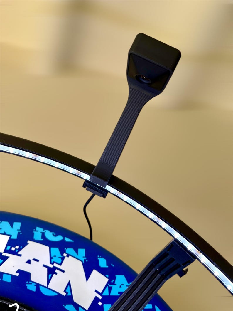 May include: A black, curved LED light with a rectangular head and a ribbed handle is attached to a blue and white object. The light is emitting a bright white glow. The object has the word "FAN" in large white letters.