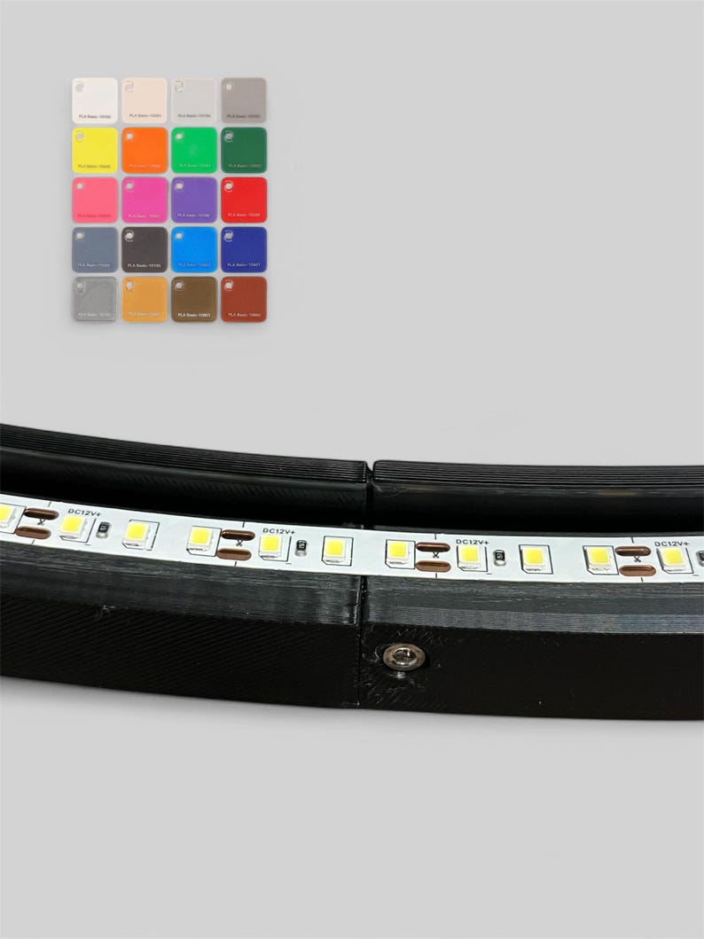 Op de afbeelding: Een zwart, gebogen LED-armatuur met een witte LED-strip. Een kleurenpalet met kleine vierkante kleurstalen bevindt zich in de linkerbovenhoek. De kleurstalen omvatten wit, beige, geel, oranje, groen, roze, paars, rood, grijs, bruin, blauw en donkerrood.