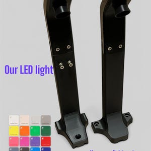 Op de afbeelding: Twee zwarte LED-armaturen met een rechthoekige basis en een cilindrische bovenkant. De tekst "Our LED light" en "Your own light system" zijn zichtbaar. Er wordt ook een kleurenpalet van verschillende kleuren getoond.