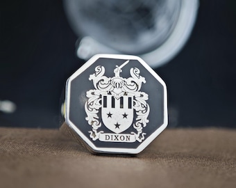 May include: An octagonal signet ring featuring a black face with a silver-toned engraved coat of arms. The crest displays a shield with three stars and vertical stripes, topped by a helmet and sword. The name DIXON is engraved below the shield.