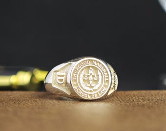 May include: A silver-toned ring featuring a circular emblem with the text THURGOOD MARSHALL SCHOOL OF LAW and a central scale of justice icon. The letters JD are engraved on the side of the band, and the text Est. 1947 is visible below the scale.
