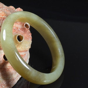 Op de afbeelding: Een lichtgroene jade armband. De armband is glad en gepolijst en ligt op een schelp.
